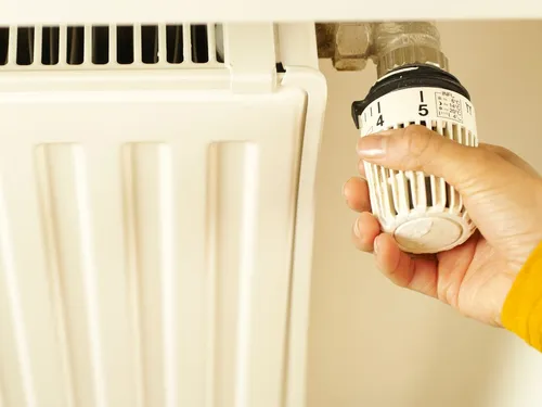 Hand adjusting a thermostatic valve on a white radiator