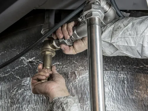 Plumber fitting brass and chrome pipework beneath a new installation